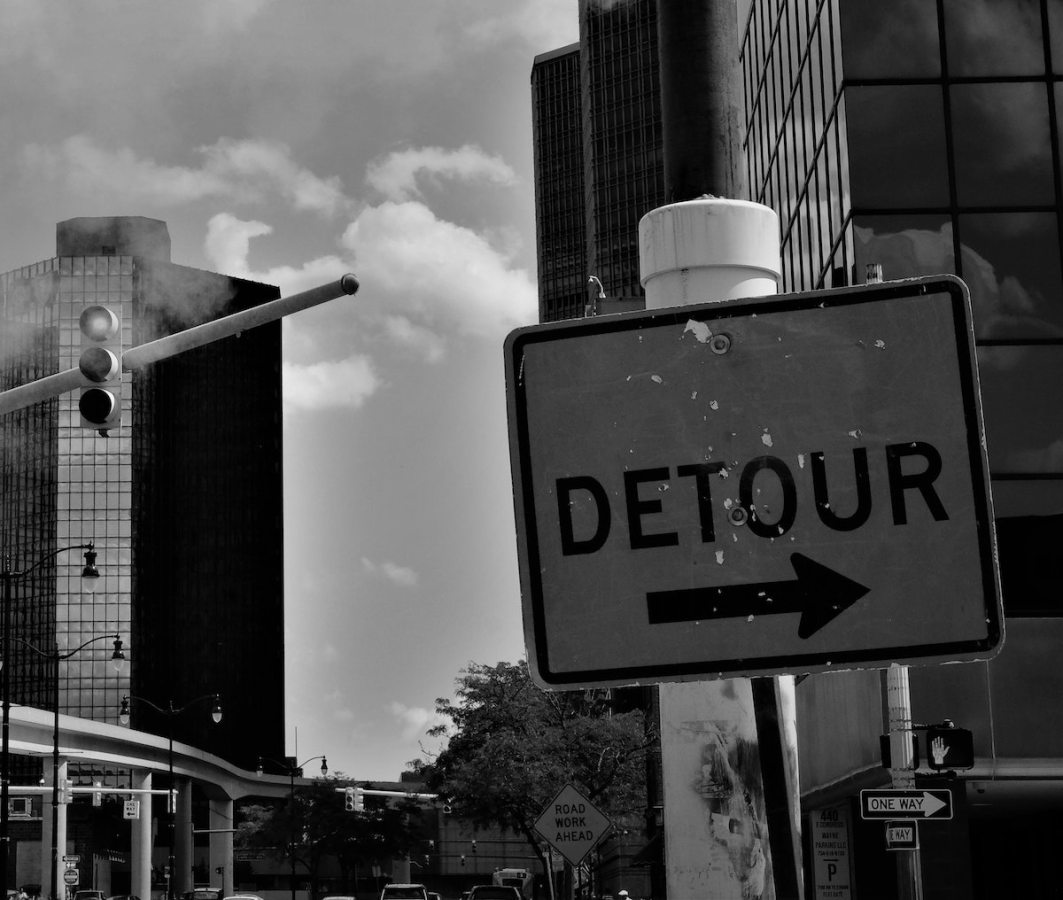 black and white photo of buildings in downtown detroit with "detour" sign in foreground